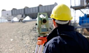 Surveyor in a hard hat using equipment during an alta title survey on land prepared for a major development project