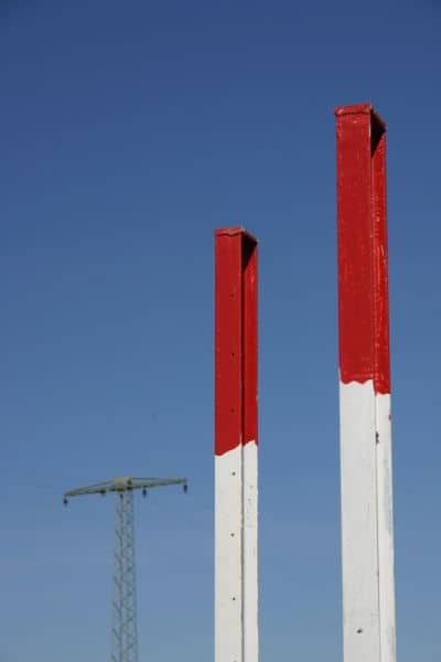Survey stakes marking land boundaries with a power line corridor in the background documented by an alta title survey
