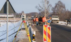 Construction surveyor setting up total station to inspect road damage after winter storm