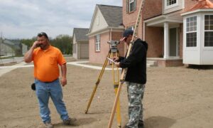 Land surveyor using a tripod to measure property boundaries near a new home