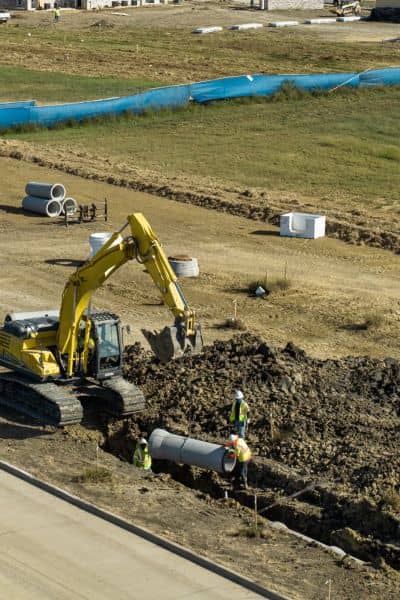 Construction crew installing underground utility pipe in a trench showing site conditions identified in an alta land survey